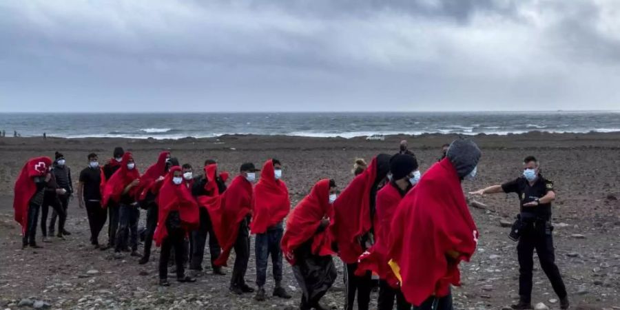 Migranten aus Marokko stehen an einem Strand auf Gran Canaria, nachdem sie den Atlantik mit einem Holzboot überquert haben. Foto: Javier Bauluz/AP/dpa