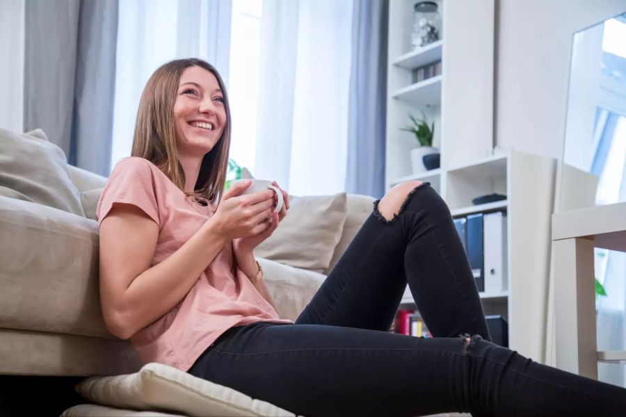 Lachende Frau sitzt vor Sofa mit Kaffee