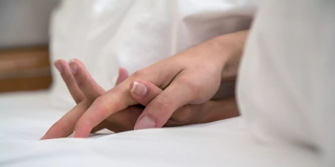 Zwei Hände Bett weisse Laken