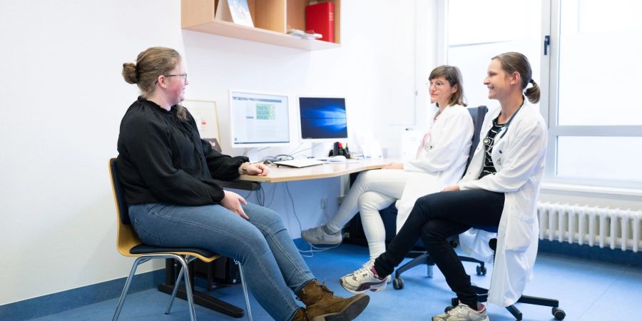 Judith Lohse (r), Kinderärztin, und Katharina Egger-Heidrich, Fachärztin Onkologie, sitzen mit einer Patientin im Nationalen Centrum für Tumorerkrankungen in einem Behandlungsraum.