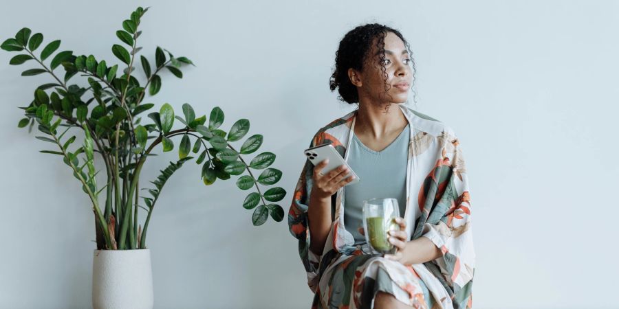 Frau sitzend mit Matcha Tee und Pflanze daneben