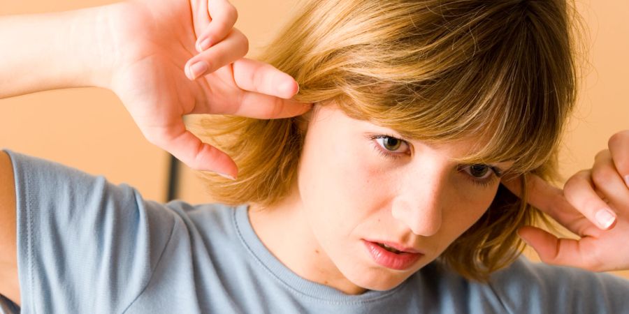 Frau mit Tinnitus hält sich die Ohren zu.