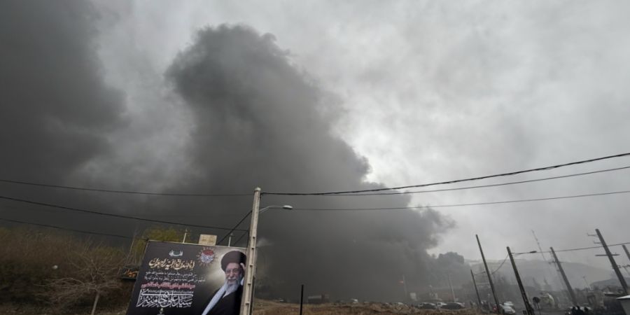Eine dicke Rauchwolke, die von einem amerikanisch-israelischen Angriff auf eine Ölanlage am späten Samstag herrührt, ist am wolkenverhangenen Himmel hinter einer Werbetafel, die den ...
