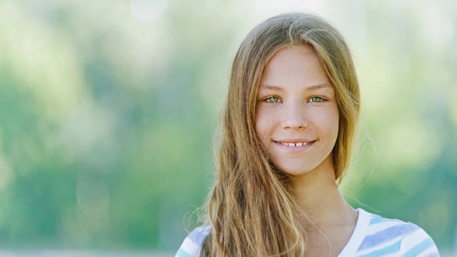 blondes teenagermädchen schaut in die kamera, grüner hintergrund, natur