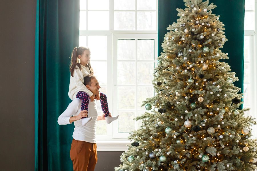 Ein Vater bewundert gemeinsam mit seiner Tochter den wunderschön in Silber und Grün dekorierten Weihnachtsbaum.