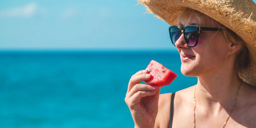 Frau am Meer isst Wassermelone