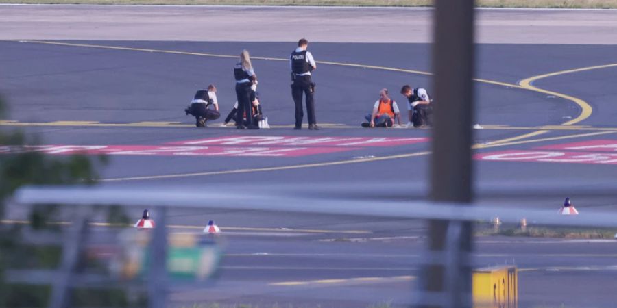 Polizisten stehen auf dem Flugfeld in Düsseldorf (D) und versuchen Aktivisten der Gruppe Letzte Generation vom Asphalt zu lösen, nachdem sie sich festgeklebt haben. (Archivbild)