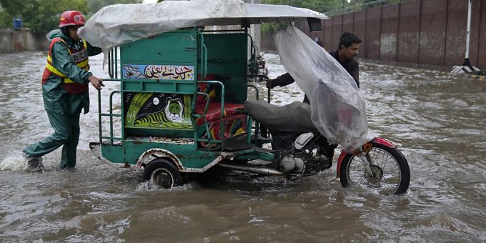 Ein Mitglied eines Rettungsteams hilft einem Mann seine Motorrad-Rikscha über eine überschwemmte Strasse zu schieben. Schwere Monsunregenfälle haben in Pakistan nach offiziellen Angaben bereits mehrere Todesopfer gefordert. (Archiv) Foto: K.M. Chaudary/AP/dpa pakistan