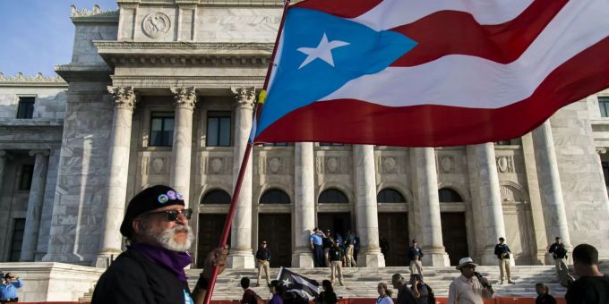 Ein Mann hält vor dem Kapitol die Flagge von Puerto Rico in die Höhe. Puerto Rico Governor