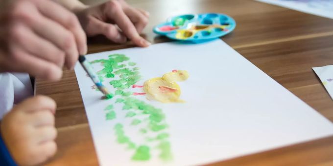 Eine Betreuerin hilft einem Kind beim Malen. Kinder