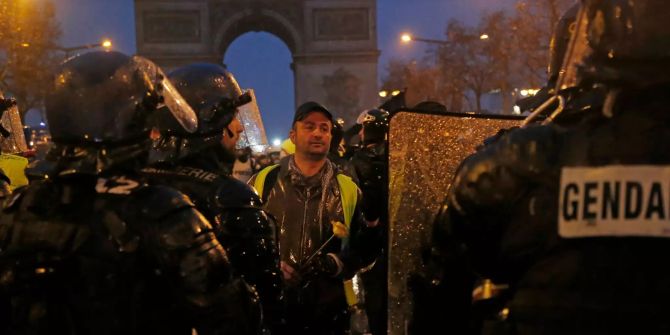 Ein «Geldwesten»-Demonstrant hält eine Blume in seinen Händen und steht vor Bereitschaftspolizisten.