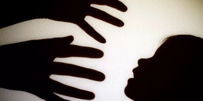 Schatten von Händen einer erwachsenen Person und dem Kopf eines Kindes an einer Wand. Kindesmissbrauch