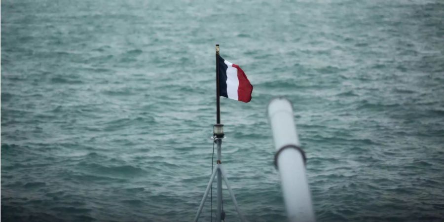 Eine französische Flagge weht auf einem Mast neben einer 100 mm Kanone auf der französischen Fregatte Prairial während eines Hafenanlaufs in Hongkong.