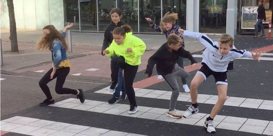 Jugendliche tänzeln über den Fussgängerüberweg «Silly Walks», an dem ein Schild dazu ermutigt, möglichst verrückt über die Strasse zu gehen.