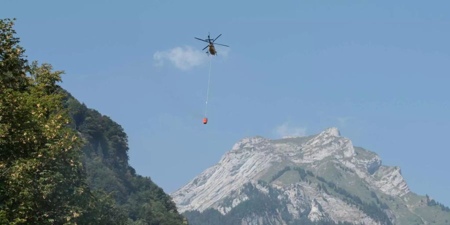 Ein Helikopter transportiert Loeschwasser um den Brandherd nach einem Kleinflugzeugabsturz am Lopper in Hergiswil im Kanton Nidwalden zu löschen.