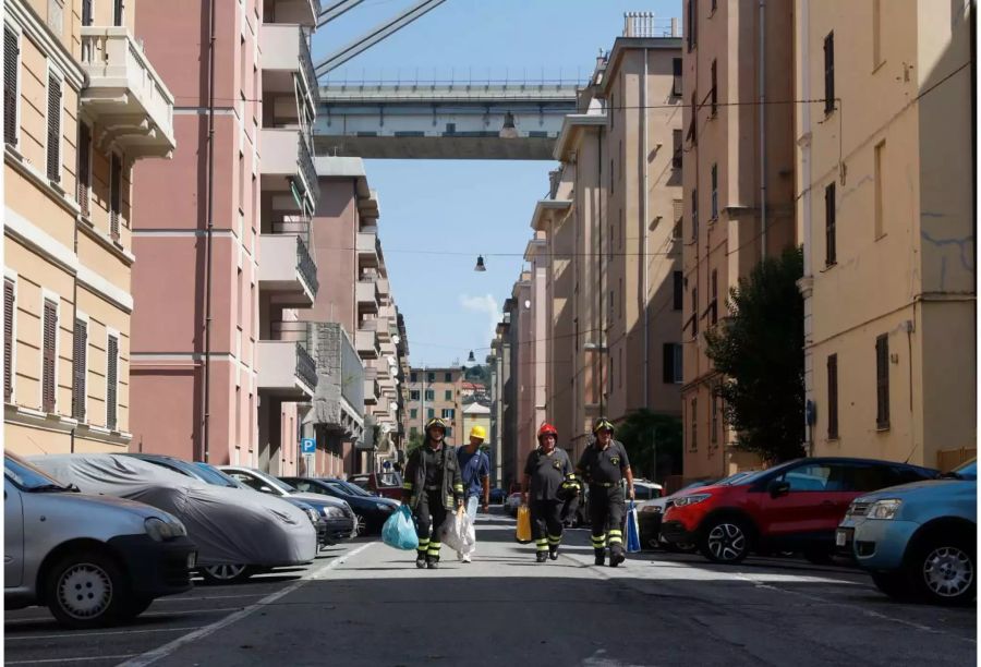 Feuerwehrmänner tragen persönliche Gegenstände von Anwohnern der evakuierten Wohnhäuser. Etwa 630 Menschen leben in den Wohnhäusern unterhalb oder neben der teilweise eingestürzten Morandi Brücke.