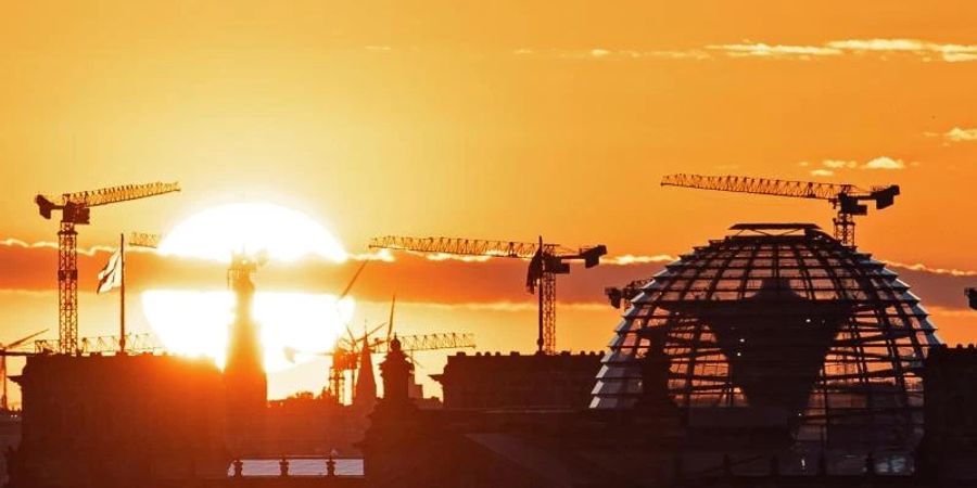 Baukräne und die Kuppel des Reichstagsgebäudes in Berlin. Die deutsche Wirtschaft kommt wieder in Schwung. Foto: Fabian Sommer/dpa