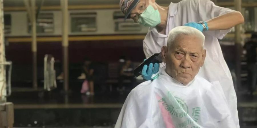 Auf dem Hauptbahnhof Hua Lamphong schneidet ein Friseur einem älteren Mann die Haare. Der Haarschnitt ist kostenlos. Foto: Christoph Sator