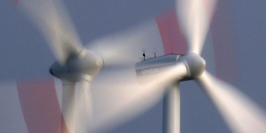 Zwei Windräder drehen sich bei heftigem Wind vor wolkenüberzogenem Himmel.
