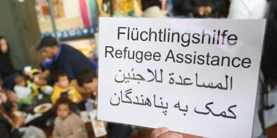 Ein freiwilliger Helfer hält 2015 im Hauptbahnhof in Hamburg ein Schild auf deutsch, englisch und arabisch, auf der Hilfe für Flüchtlinge angeboten wird. Foto: Bodo Marks/dpa