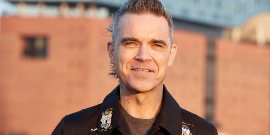 Robbie Williams, britischer Sänger und Songwriter, während eines Fototermins auf einer Barkasse im Hamburger Hafen. Im Hintergrund ist die Elbphilharmonie zu sehen.