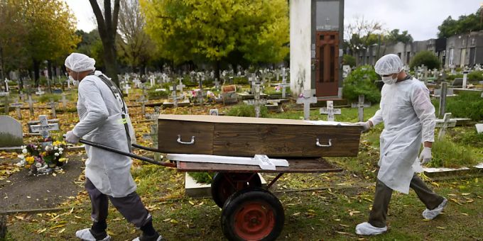 Zwei Männer in Schutzanzügen transportieren den Sarg mit dem Leichnam eines Corona-Opfers. Argentinien