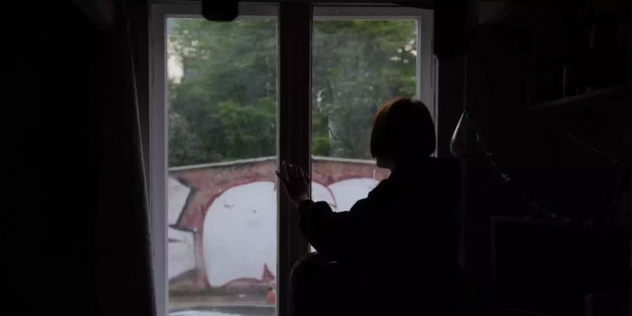 Eine Jugendliche sitzt in einem abgedunkelten Zimmer am Fenster. Foto: Paul Zinken/dpa