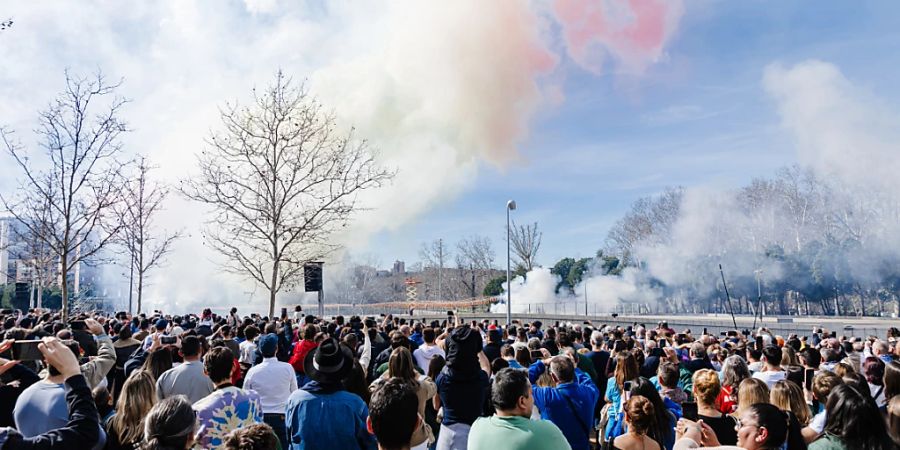 Zuschauer beobachten den bunten Rauch während der ersten Madrider Mascleta auf der Puente del Rey. Bei der Veranstaltung, die von der Pirotecnia Valenciana durchgeführt wird, werden 300 Kilo Schiesspulver für insgesamt sieben Minuten mit 3.000 Detonationen gezündet. Die Regierungsdelegation hat die Mascleta schliesslich genehmigt, obwohl Umweltschutz- und Umweltorganisationen vor Gericht geklagt haben. Foto: Carlos Luján/EUROPA PRESS/dpa