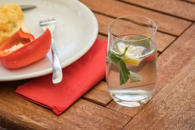 Gegen ein Getränk zum Essen ist nichts einzuwenden. Die Magensäure wird nämlich erst bei grösseren Mengen Flüssigkeit so verdünnt, dass sich das bemerkbar macht. Glas Wasser Zitrone Teller Essen