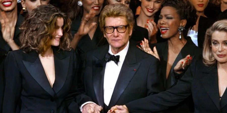 Designer Yves Saint Laurent (m.) mit Model Laetitia Casta (l.) und Schauspielerin Catherine Deneuve (r.) 2002 in Paris. Foto: Jean-Pierre Muller/AFP/dpa