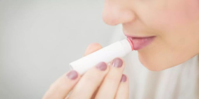 Gegen trockene Lippen helfen Lippenbalsam und Hausmittel. Frau hält Lippenbalsam in der Hand