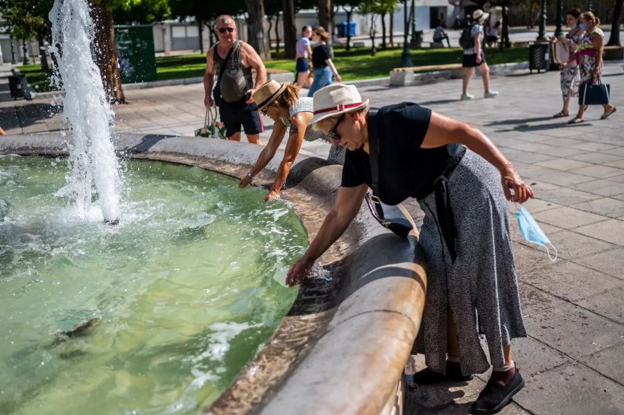 31.07.2021, Griechenland, Athen: Touristen erfrischen sich bei Temperaturen über 40 Grad mit Wasser aus einem Brunnen auf dem Syntagma-Platz.