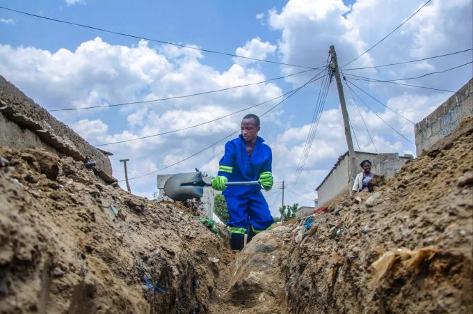Laufende Bauarbeiten für das neue Leitungsnetz in Gondwe, Lusaka, Sambia. Mann bei Bauarbeiten