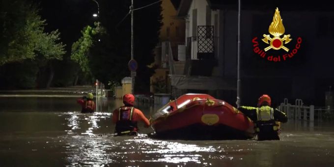 Feuerwehrleute von Senigallia schieben ein Schlauchboot durch eine überflutete Strasse, um Menschen aus den Häusern zu retten. Überschwemmung