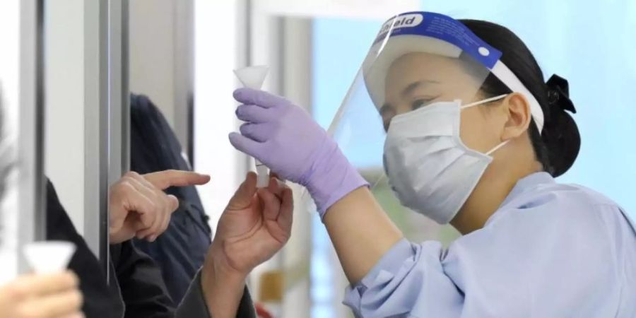 Eine Quarantänebeamtin sieht sich am Flughafen Tokio-Narita kurz nach Weihnachten eine Speichelprobe für einen Corona-Antigentest von einem Passagier an, der aus Übersee angereist ist. Foto: -/kyodo/dpa