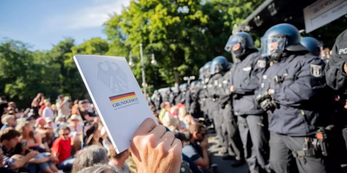Ein Teilnehmer hält bei einer Kundgebung gegen Corona-Beschränkungen vor Polizisten das Grundgesetz in die Höhe. Demonstration gegen Corona-Beschränkungen