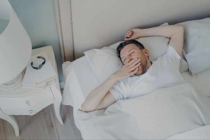 Wer die Snooze-Taste drückt, riskiert einen fragmentierten Schlaf, der müde macht. Mann erwacht morgens