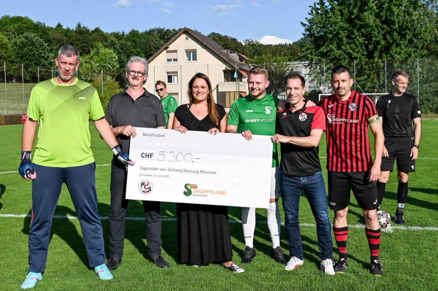 Stefan Meier (Stiftungsratspräsident), Rena Schlup (Shoppyland), Joël Wissmann (Shoppyland) und Matthias Blaser (Vizepräsident FC Schönbühl) mit dem Scheck über CHF 5'300 zugunsten der Stiftung Nutzung Moossee, umrahmt von weiteren Spielern der Teams.