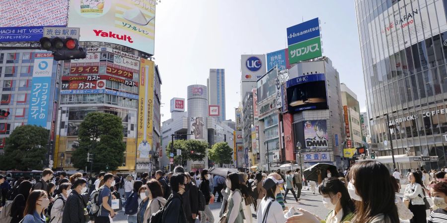 Menschen gehen im japanischen Tokio über eine Kreuzung.