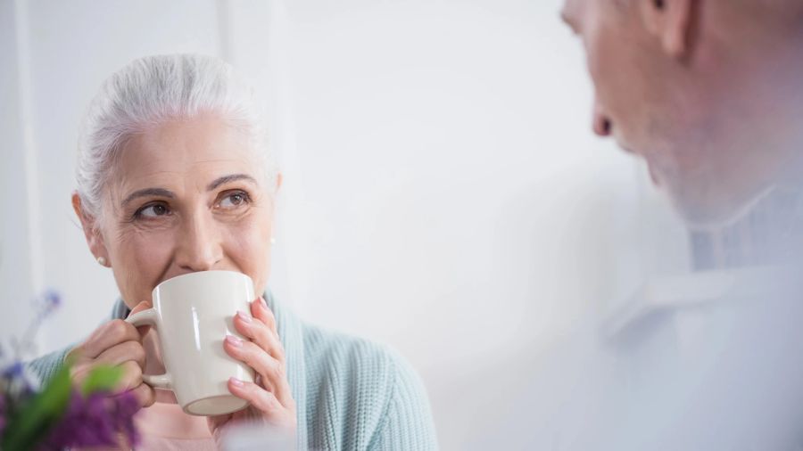 ältere dame nippt an kaffee, schaut jemanden an, weisser hintergrund