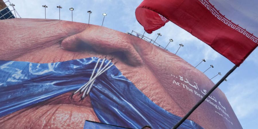 ARCHIV - Ein Mann schwenkt in Teheran eine iranische Flagge vor einer Plakatwand mit einer Darstellung der Straße von Hormus und zugenähten Lippen von US-Präsident Trump. Foto: Vahid...