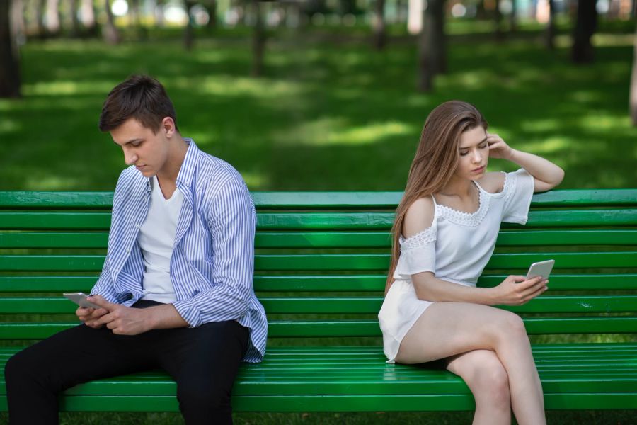 paar sitzt mit handy in der hand gelangweilt auf der parkbank