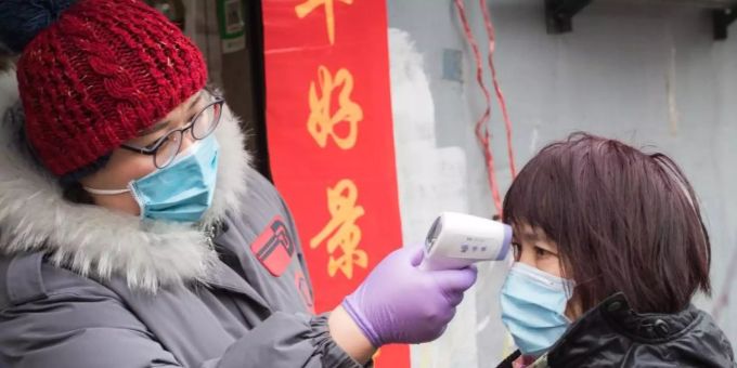 Eine Gemeindemitarbeiterin misst mit einem Fieberthermometer die Körpertemperatur einer Passantin in einer Strasse in Wuhan. Foto: Xiao Yijiu/XinHua/dpa Coronavirus Wuhan
