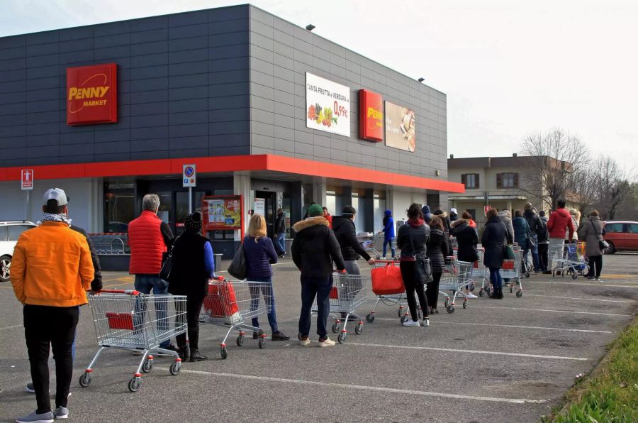 Menschen tragen Atemschutzmasken und stehen vor einem Supermarkt in einer Schlange.