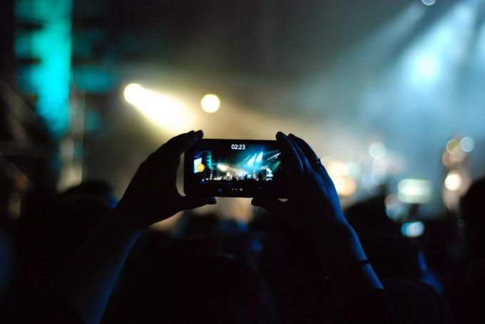 Eine Person fertigt an einem Konzert eine Videoaufnahme mit dem Smartphone an. Konzert