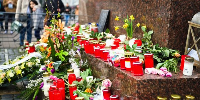 Menschen stehen um das Brüder Grimm Denkmal, an dem Blumen und Kerzen niedergelegt worden sind. Hanau