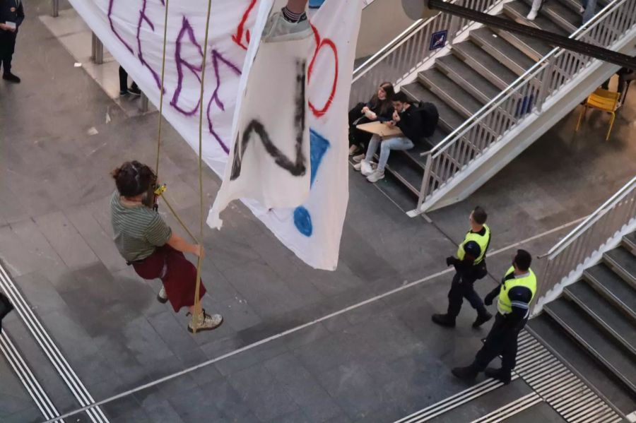 Eine Demonstrantin hängt über den Köpfen der Pendler im Bahnhof Bern.