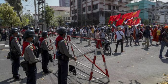 Studenten und Lehrer protestieren auf den Strassen Myanmars und werden dabei von der Polizei beobachtet. Myanmar