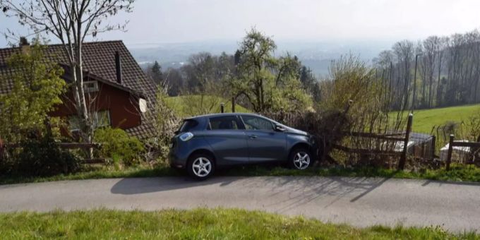 Blauer Personenwagen steht seitlich in einem Holzzaun.
