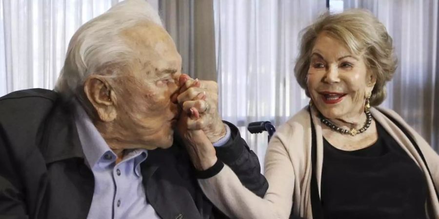 Kirk Douglas küsst die Hand seiner Frau Anne während einer Party zu seinem 100. Geburtstag. Foto: Reed Saxon/AP/dpa